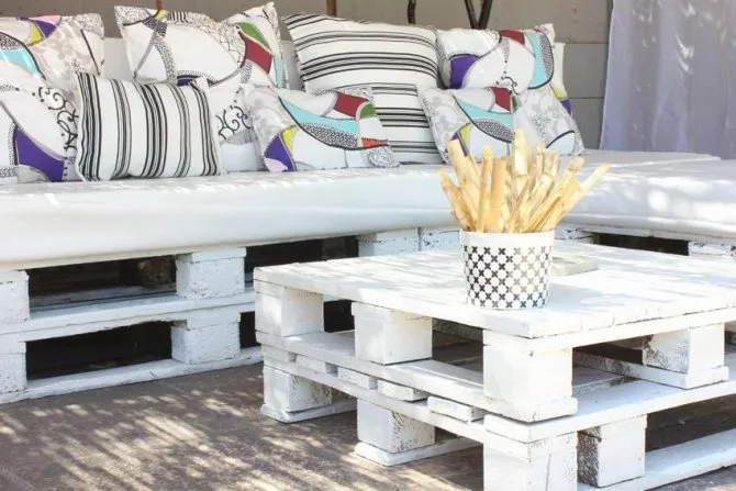 Покрашенная белой краской скамейка из европоддонов с мягким сиденьем и подушками